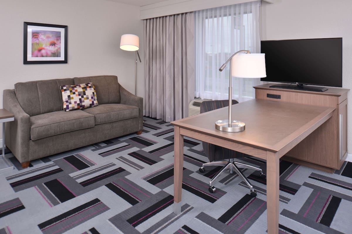 A hotel room with a sofa, a desk, a TV, and a lamp.