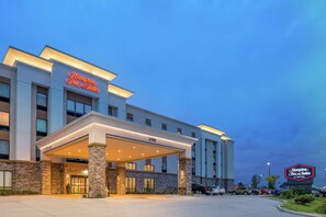 A Hampton Inn & Suites hotel with a modern design, featuring a covered entrance and a prominent address sign.