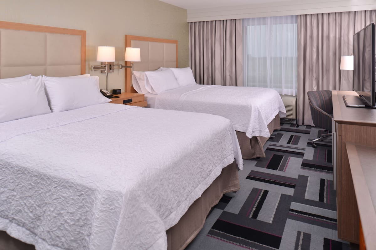 A hotel room with two beds, a desk, a chair, a television, and a window with curtains.