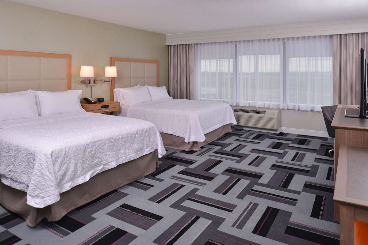 A hotel room with two beds, a desk, a chair, a television, and a window with curtains.