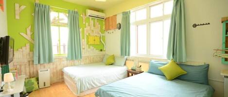 A room with two beds, a window, a wall-mounted air conditioner, and a small table with a lamp.