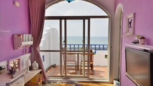 A room with a large sliding glass door leading to a balcony with a view of the sea. There is a wooden table and chairs on the balcony, and a television on the right side of the room. - Sea House homestay (Magong)