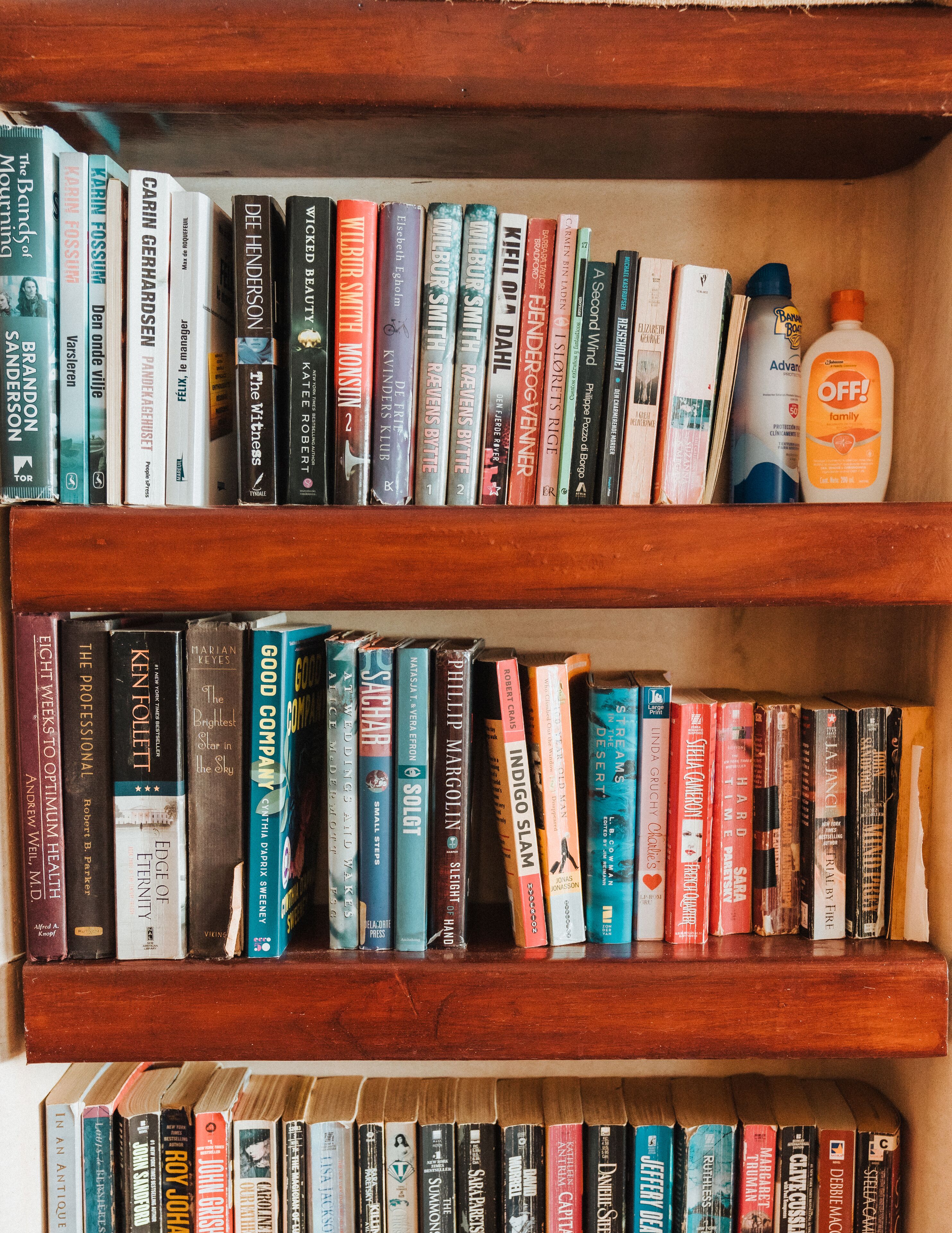 A bookshelf with a variety of books and a bottle of lotion.