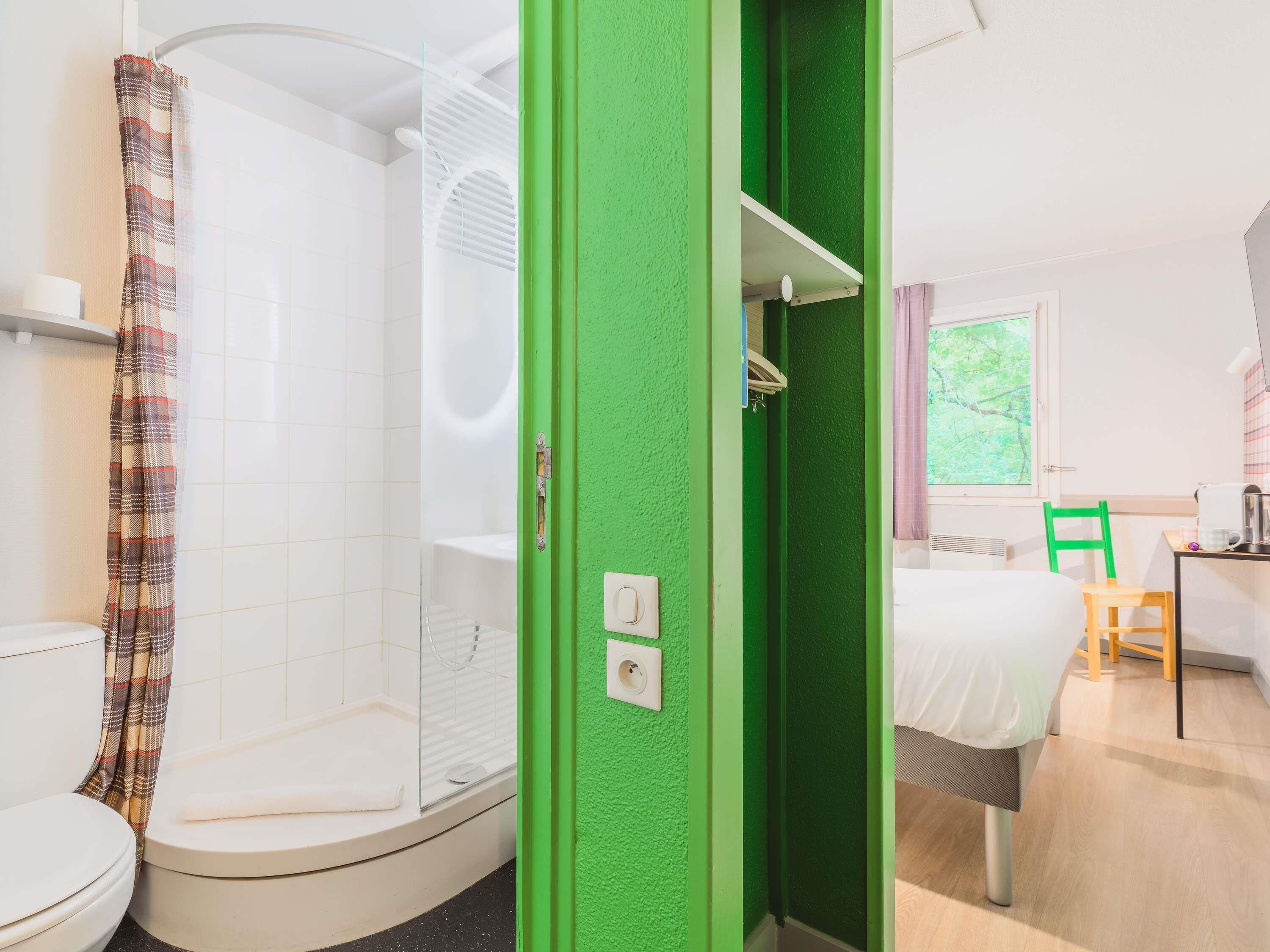 A bathroom with a shower, toilet, and a green wall.