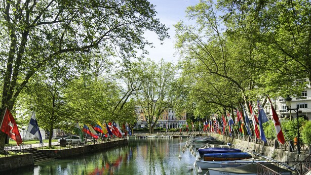 A canal with boats docked on one side, surrounded by trees and flags. - greet hotel Annecy Cran Gevrier (Annecy)