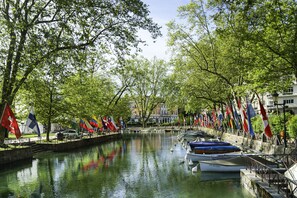 A canal with boats docked on one side, surrounded by trees and flags. - greet hotel Annecy Cran Gevrier (Annecy)