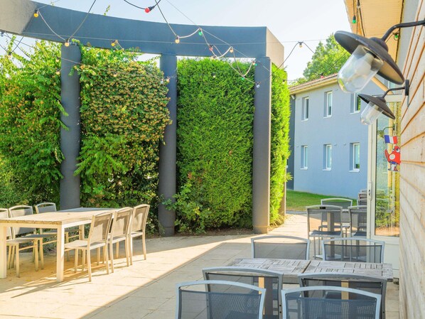 An outdoor patio with tables and chairs, a pergola with string lights, and a wall covered in climbing plants.