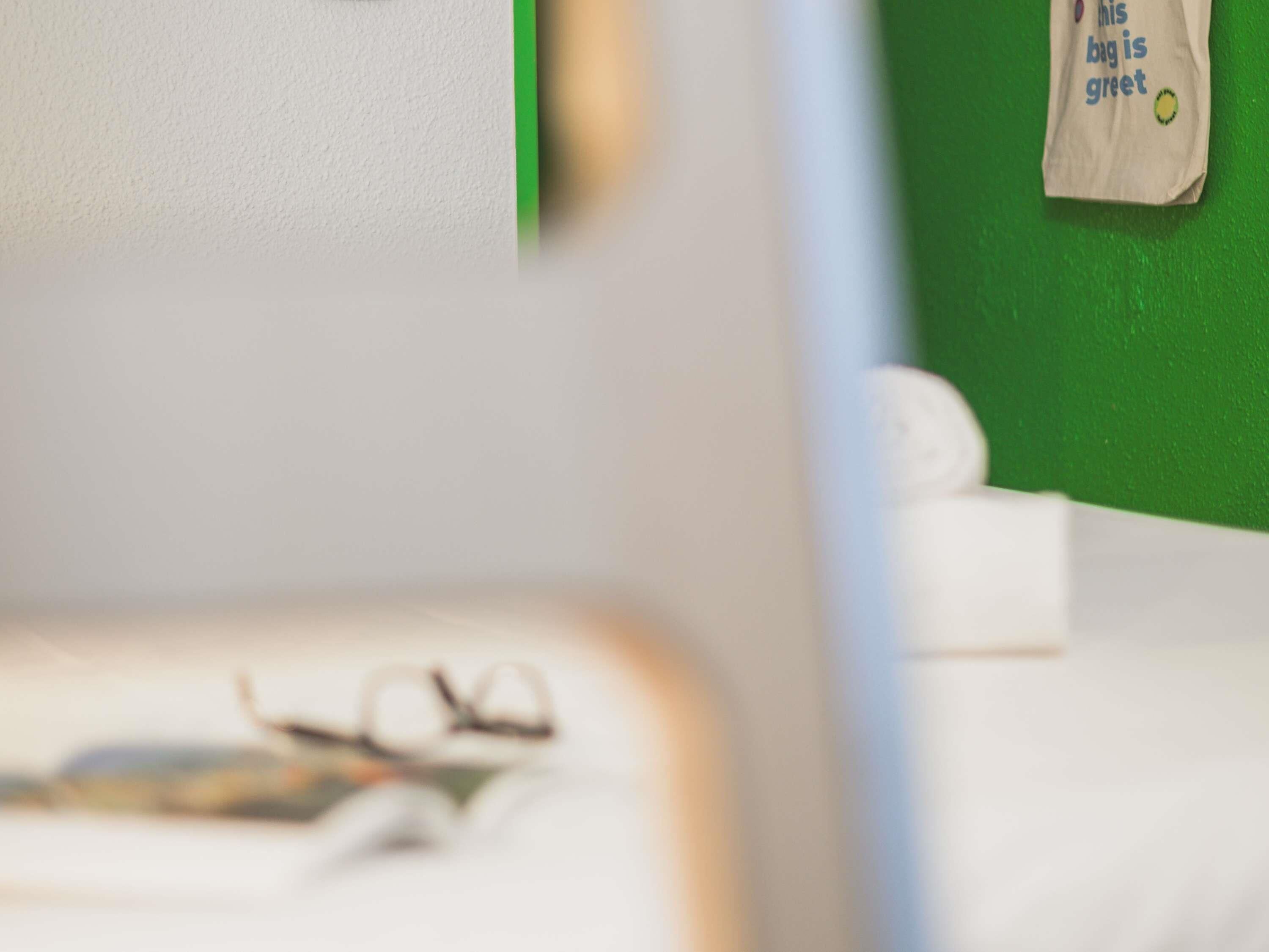 Un primo piano di una stanza con una parete verde, un letto bianco con un cuscino bianco e un paio di occhiali sul letto.