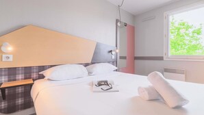 A neatly made bed with white linens, a bedside table with a lamp, and a window with a view of green trees. - greet hotel Annecy Cran Gevrier (Annecy)