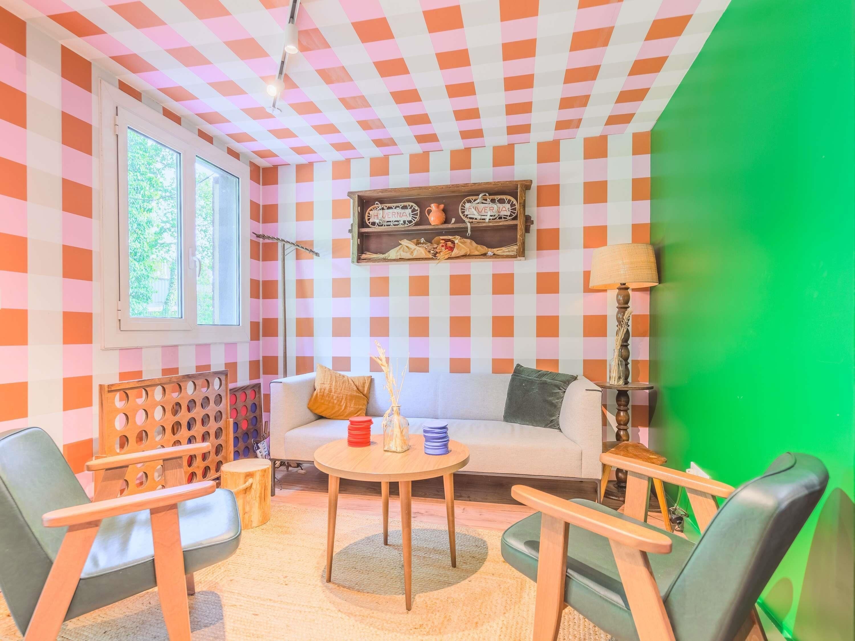 Una habitación con un estampado de cuadros en la pared, un sofá, una mesa redonda y una lámpara.