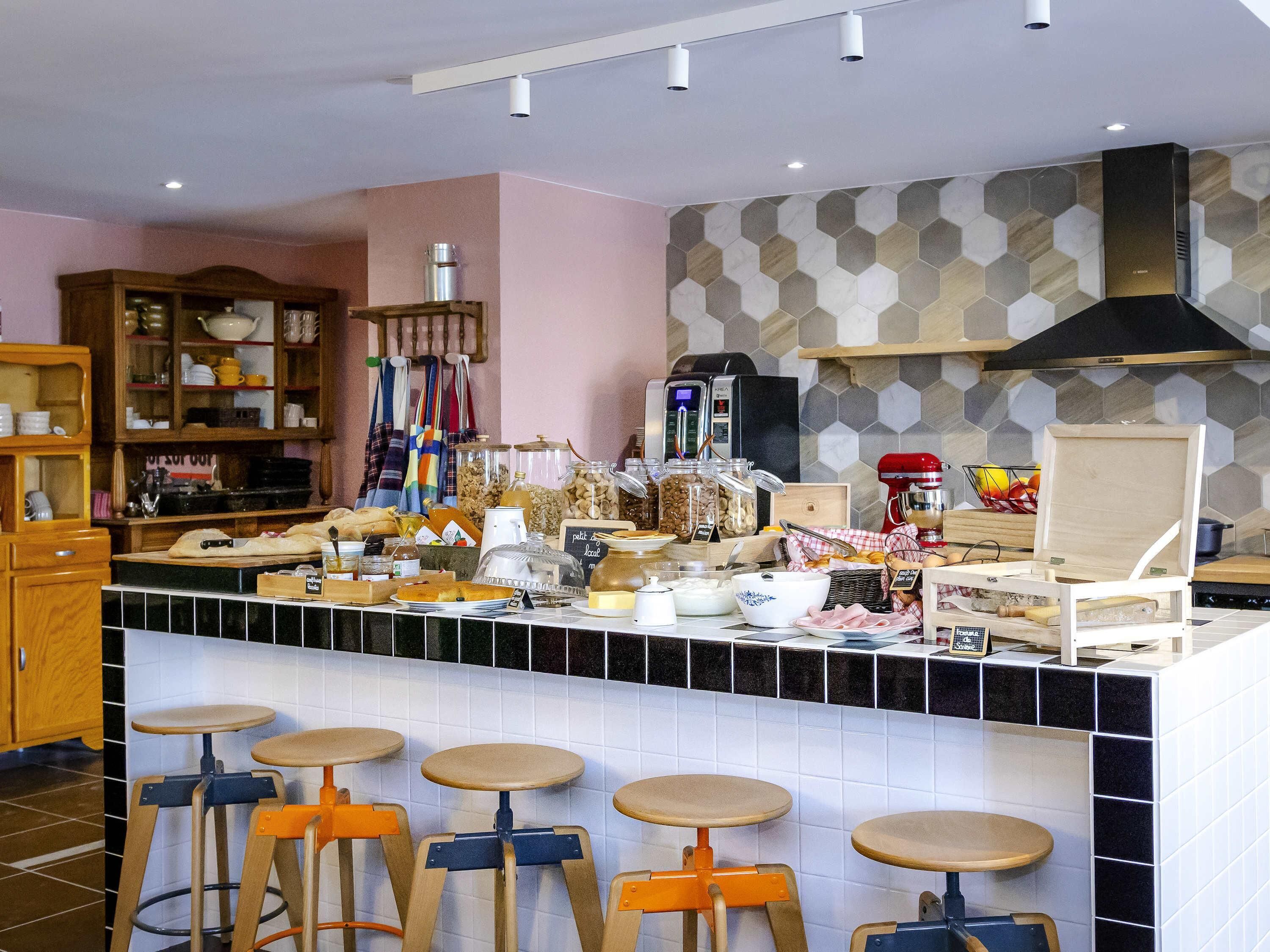 A kitchen with a central island, bar stools, a coffee machine, and various food items.