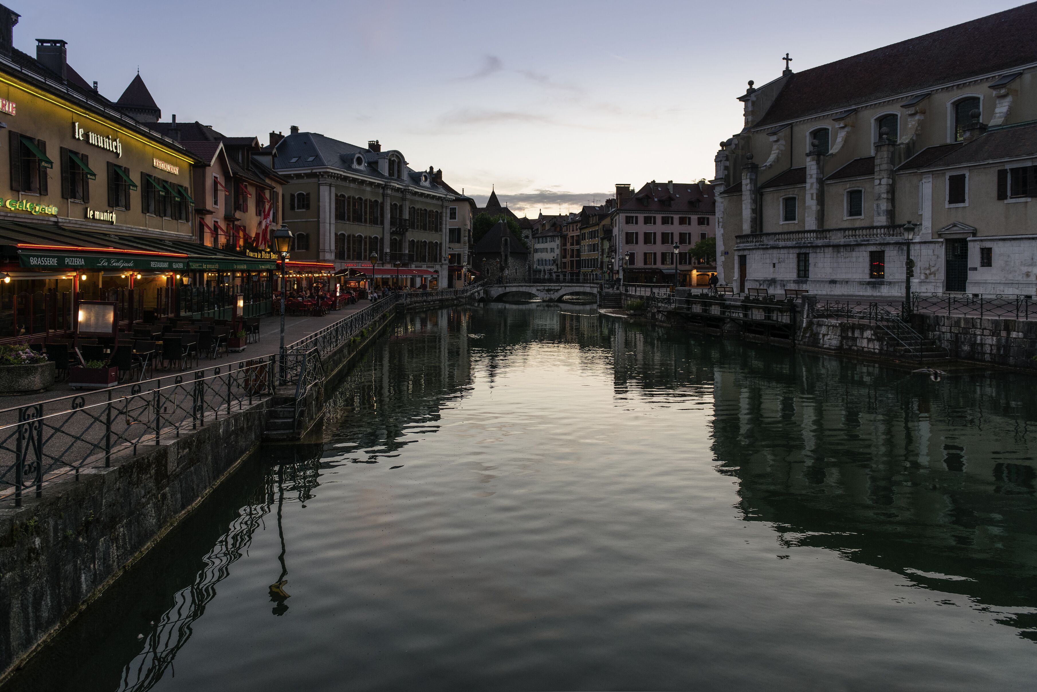 Un canal bordé de bâtiments de part et d’autre, un pont en son centre et une surface d’eau calme qui reflète les bâtiments.