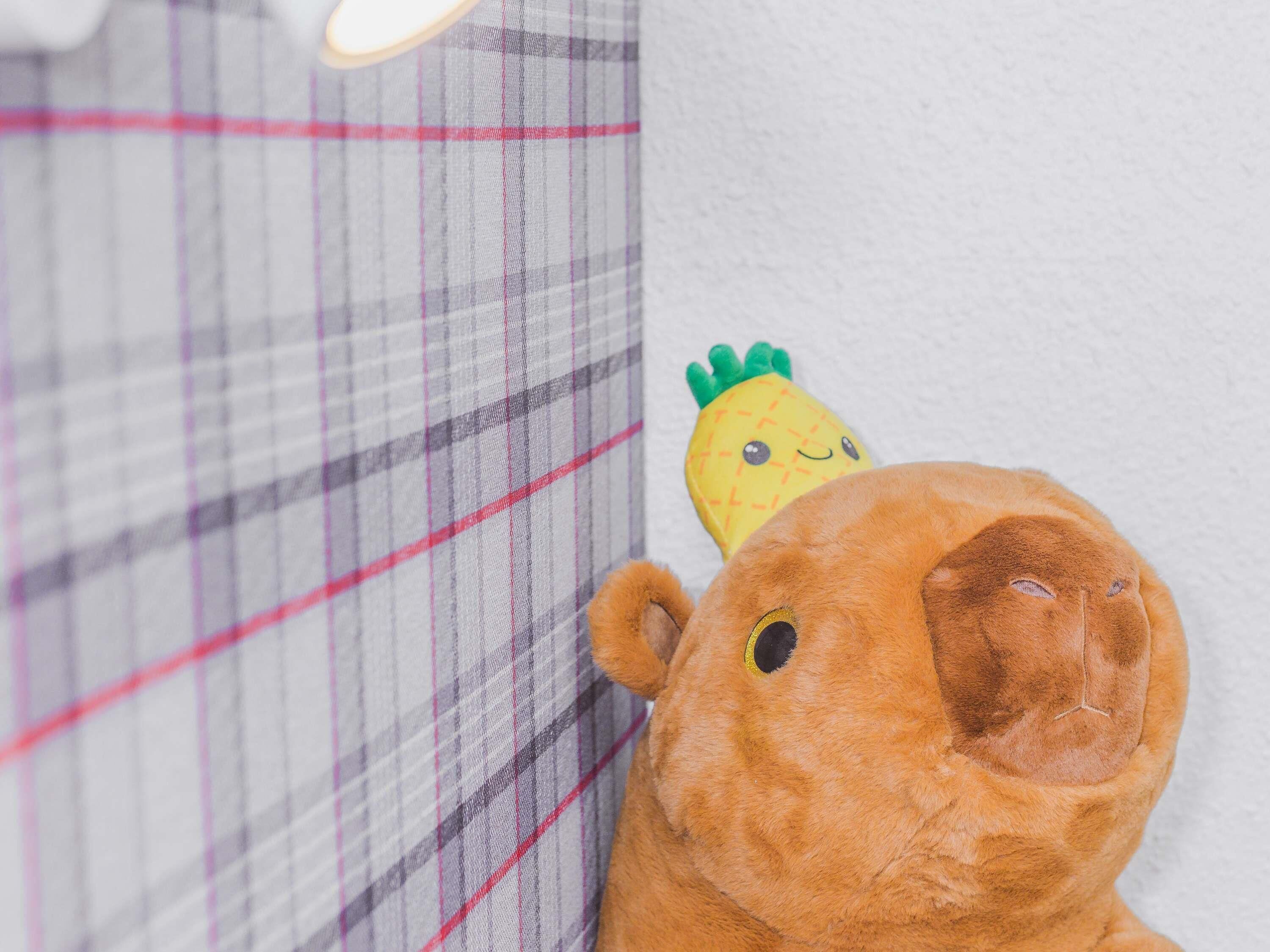 Un peluche con cabeza de piña y cuerpo marrón, situado junto a un tejido escocés con una franja roja.