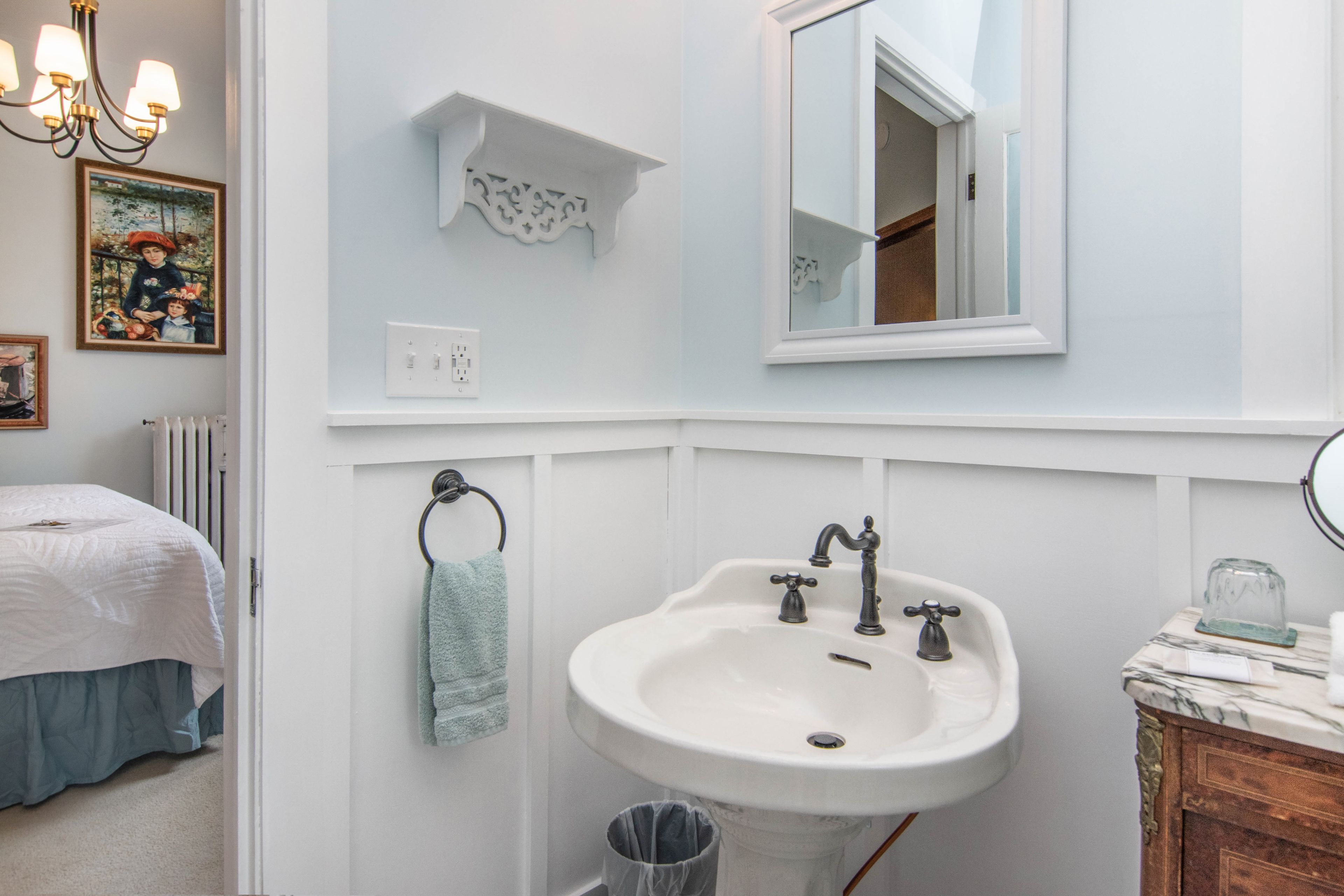 Une salle de bain avec un lavabo blanc, un miroir et un lustre.