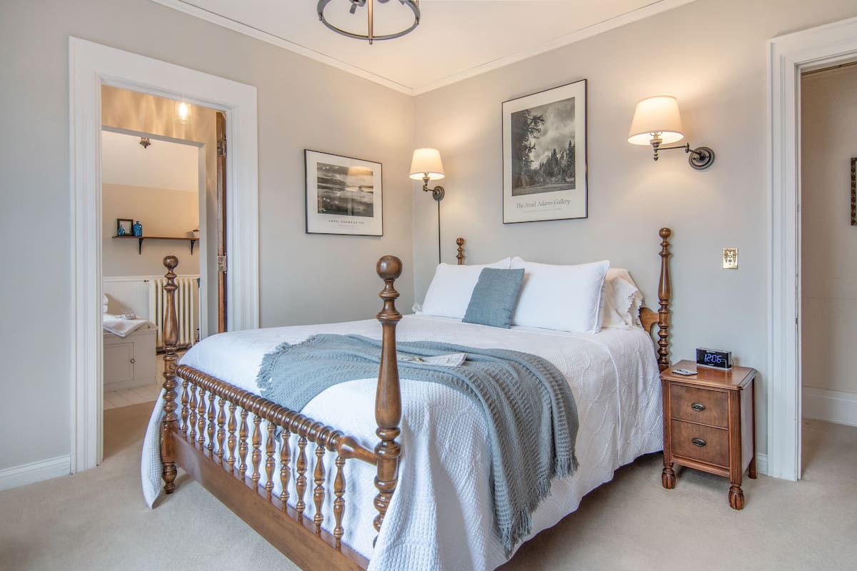 Een slaapkamer met een houten baldakijnbed, een nachtkastje met een klok en wandlampen.