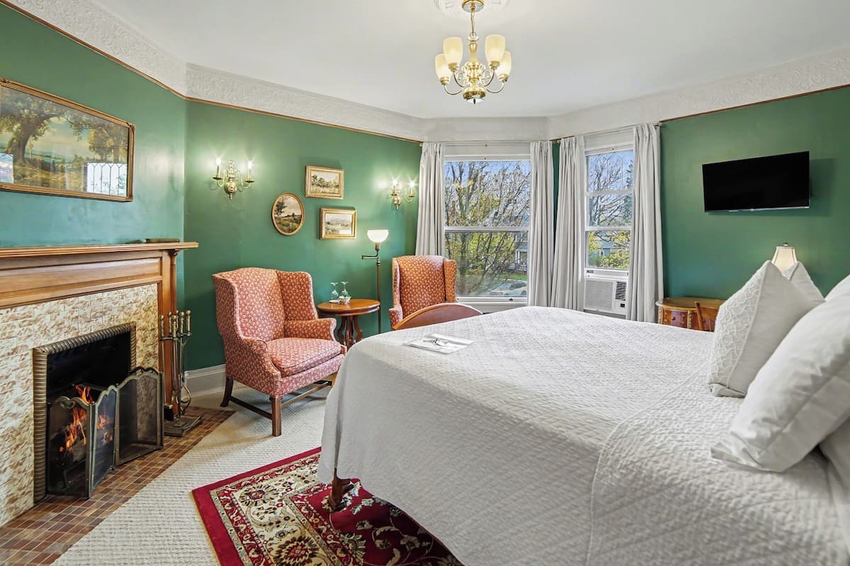 Een slaapkamer met een open haard, een bed, twee stoelen, een televisie en een raam met gordijnen.