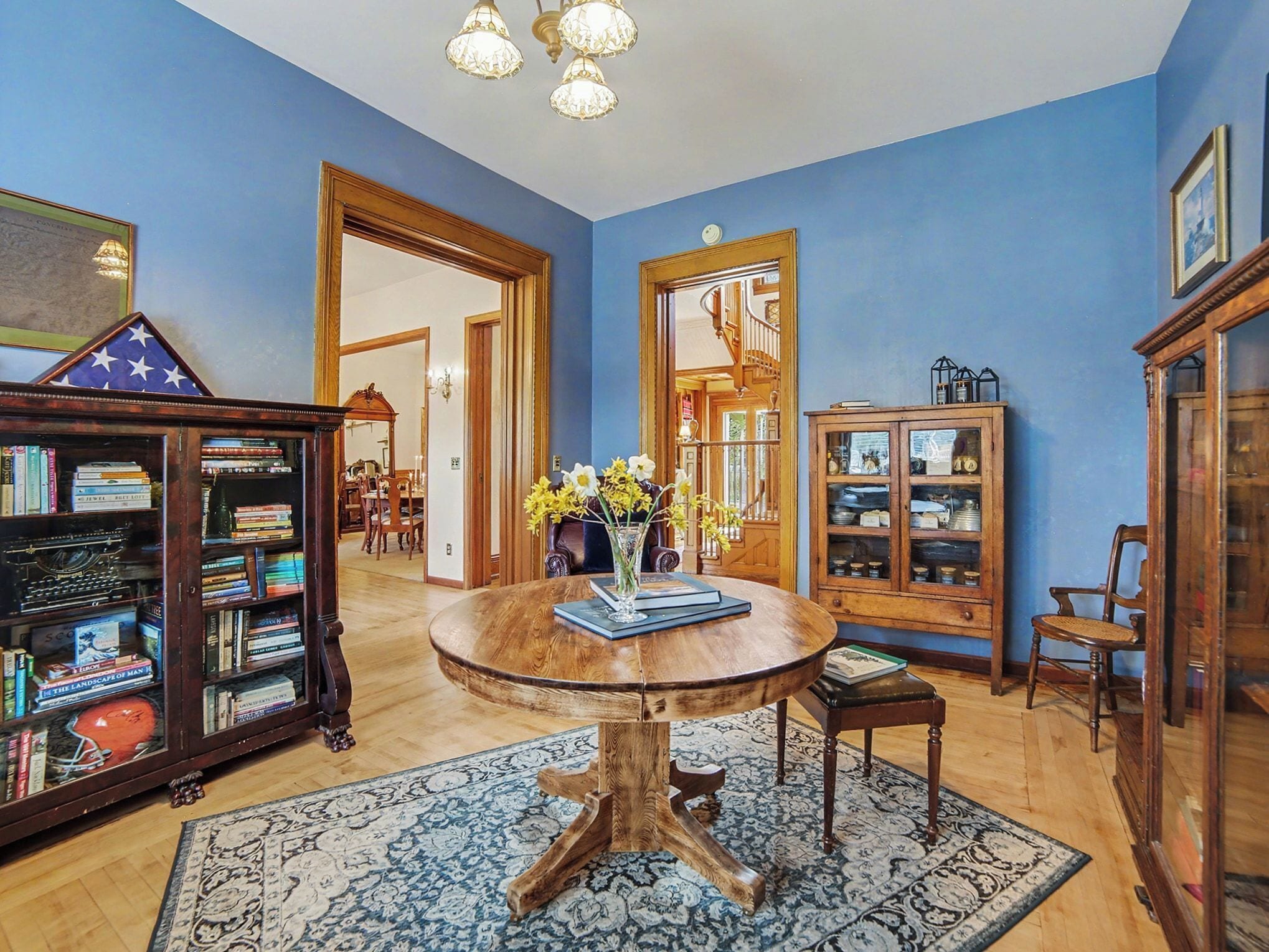 Een kamer met een houten tafel, boekenkasten, een spiegel en een kroonluchter.