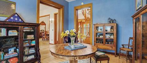 Une pièce avec une table en bois, des étagères, un miroir et un lustre.