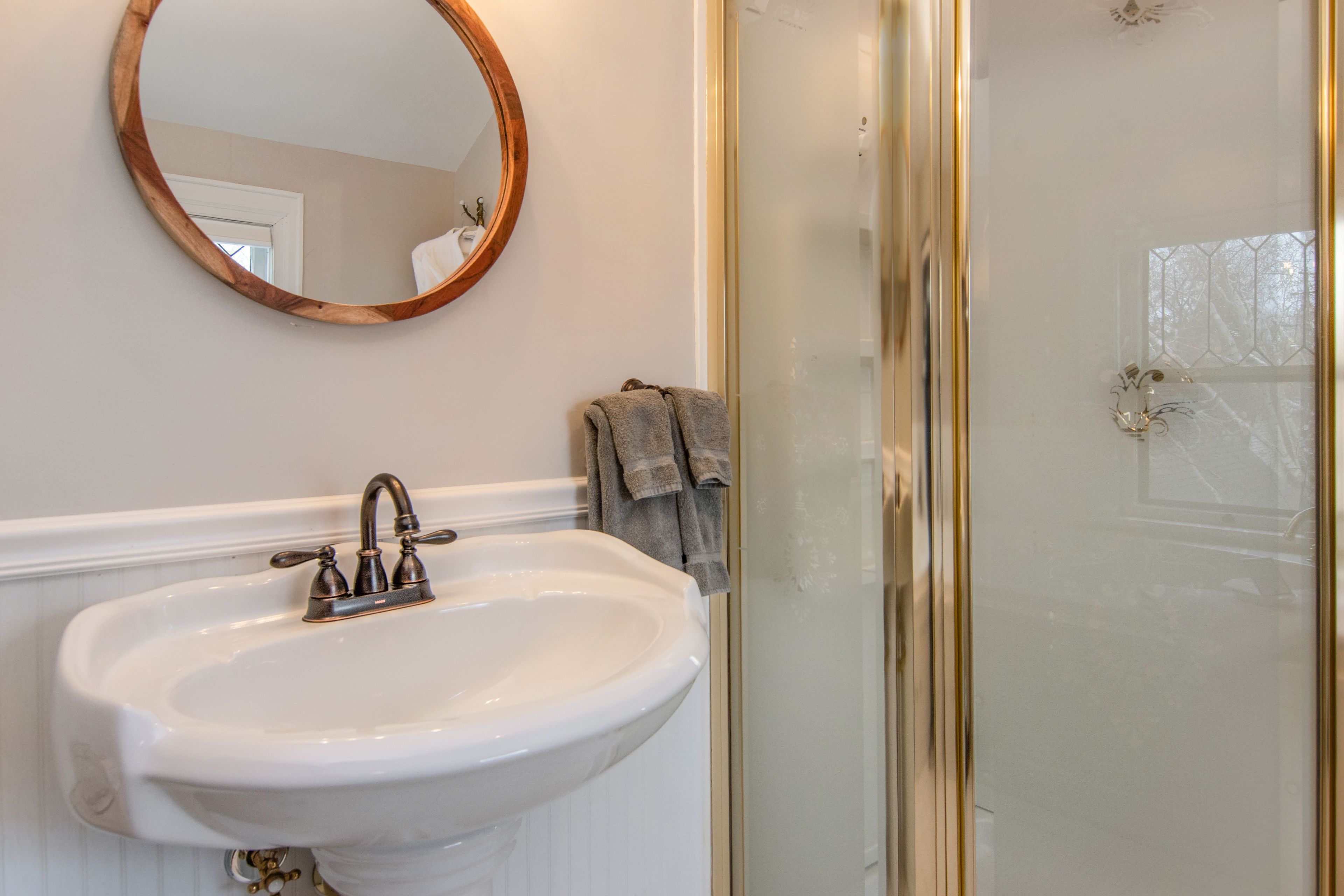 Un baño con un lavamanos blanco, un espejo con marco de madera y una puerta de ducha de cristal.