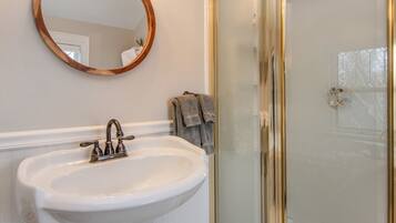 Un baño con un lavamanos blanco, un espejo con marco de madera y una puerta de ducha de cristal.