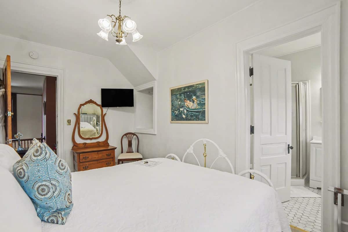 Een slaapkamer met een bed, een dressoir, een spiegel, een schilderij en een televisie aan de muur.