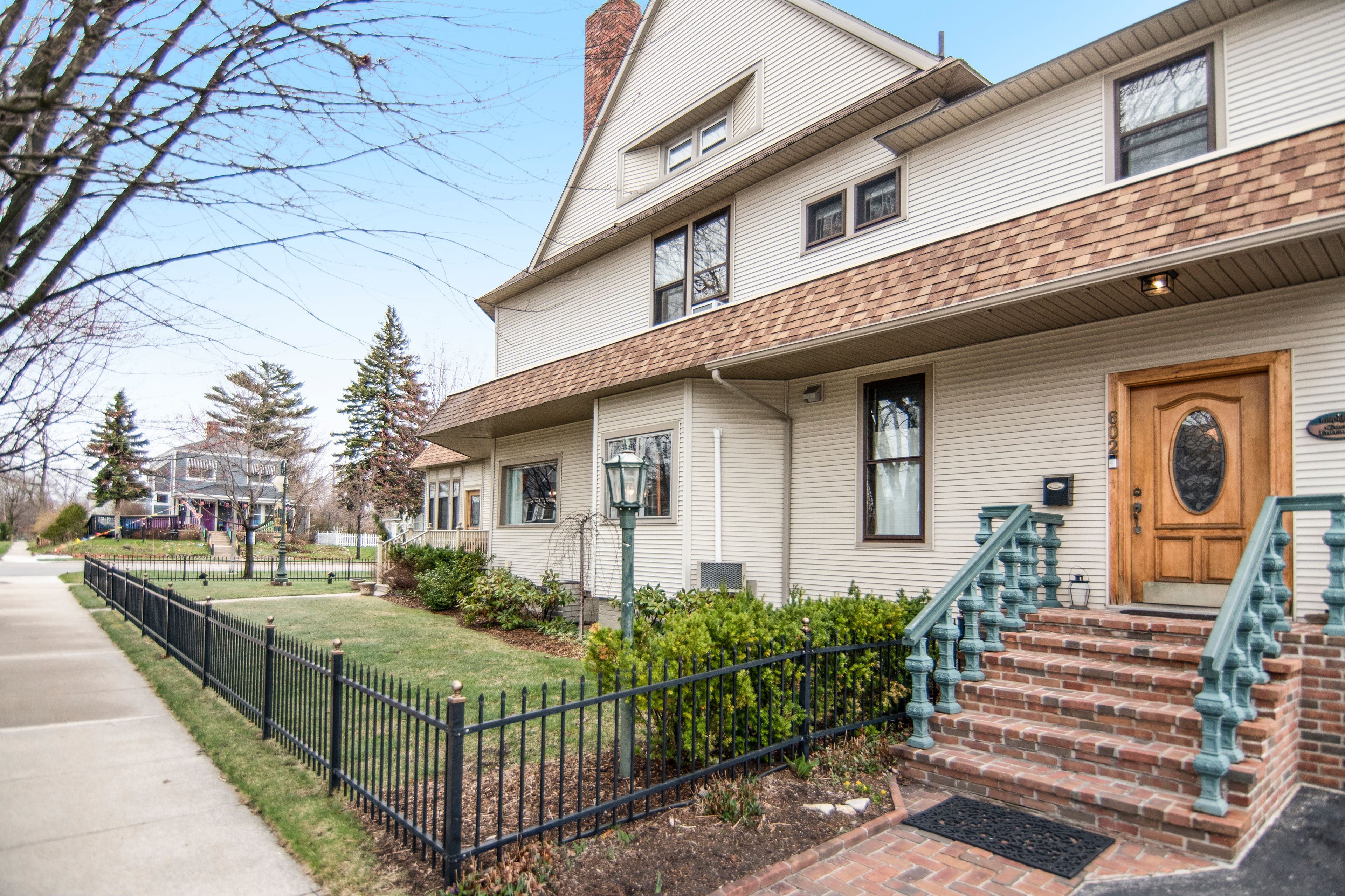 A two-story house with a front porch, a brick staircase, and a black metal fence.