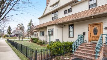 A two-story house with a front porch, a brick staircase, and a black metal fence.
