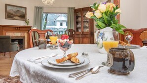 Una mesa de comedor dispuesta con alimentos para el desayuno, como cruasanes, fruta y una jarra de jugo de naranja.