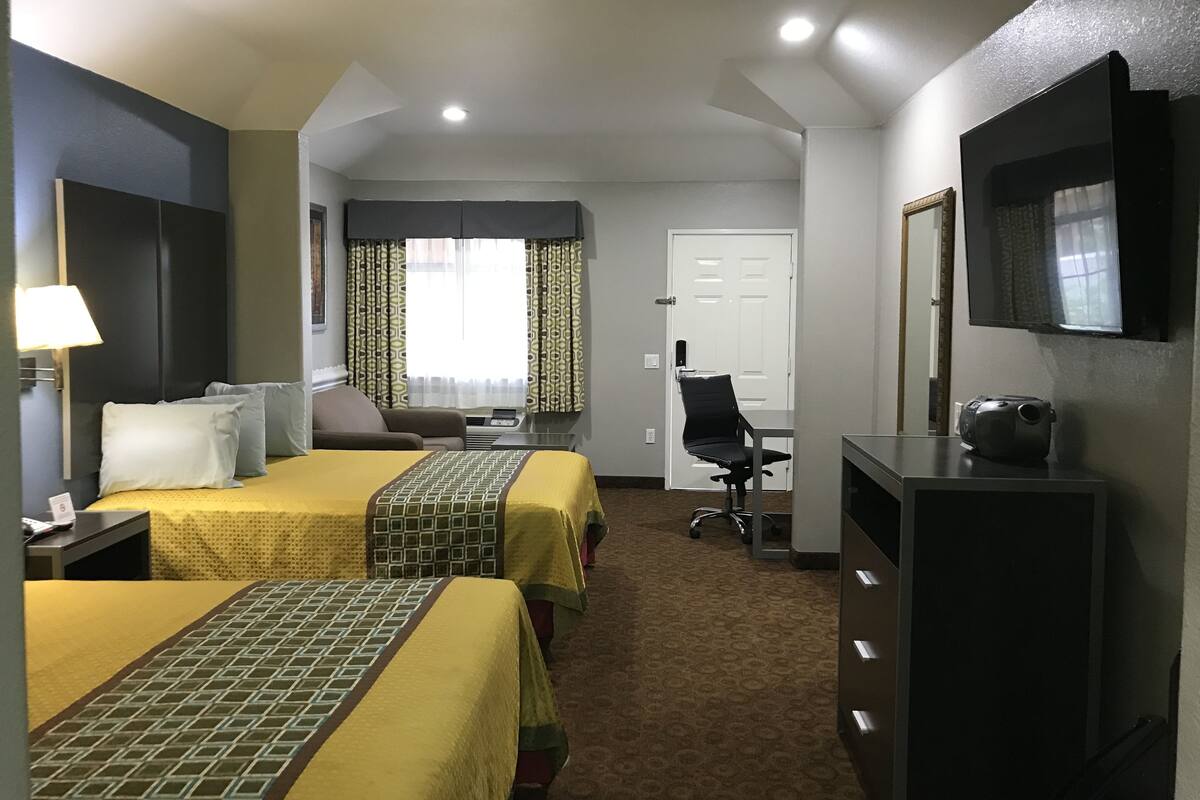A hotel room with two beds, a desk, a chair, a TV, and a mirror.