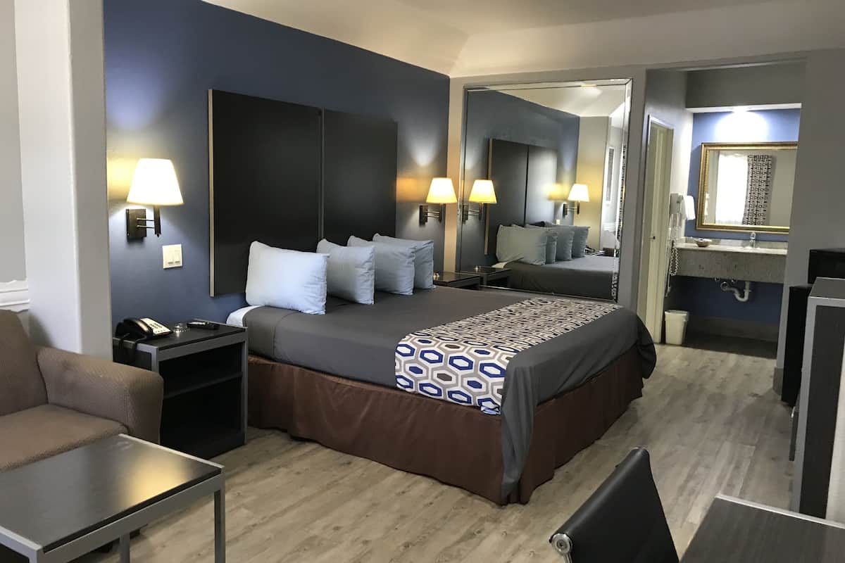 A hotel room with a large bed, bedside lamps, a desk, a chair, and a bathroom with a mirror and sink.