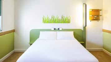 A hotel room with a bed, a wall-mounted light fixture, and a green accent wall.