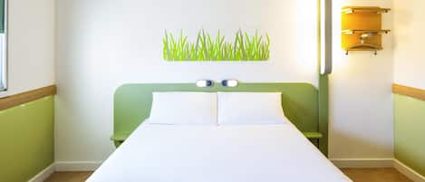 A hotel room with a bed, a wall-mounted light fixture, and a green accent wall.