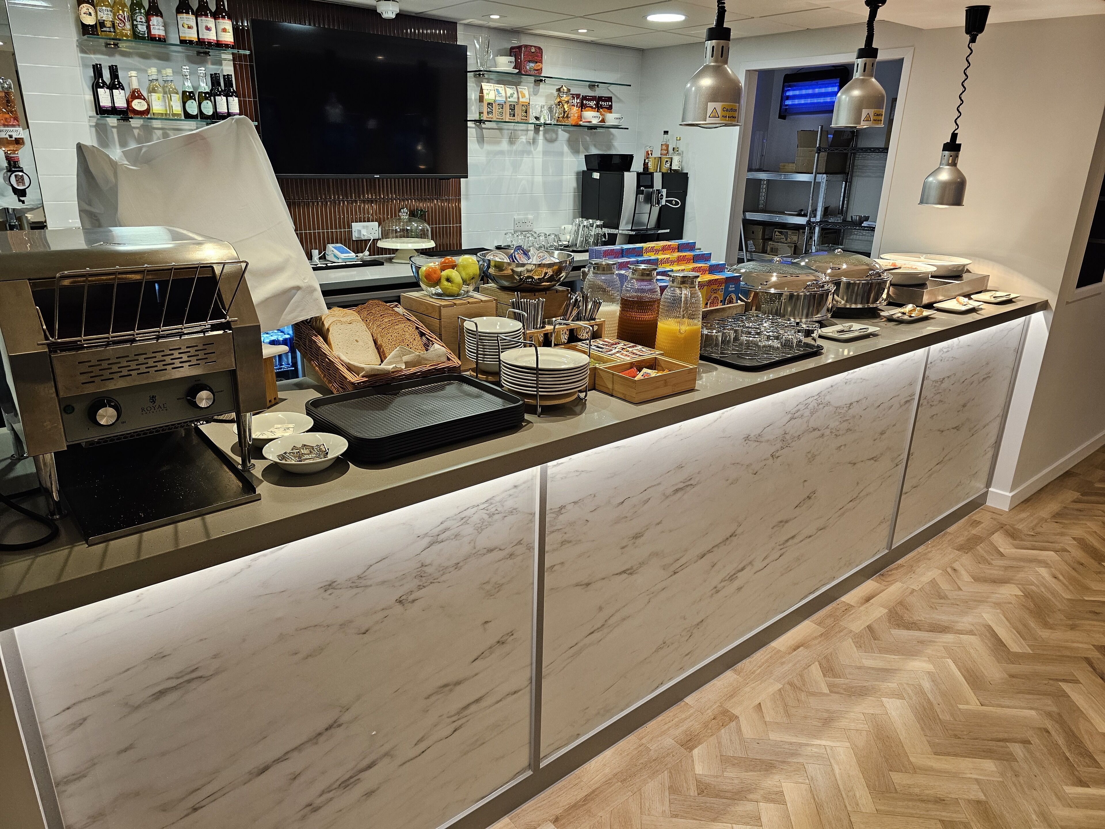 A breakfast bar with a coffee machine, bread, fruits, and beverages.