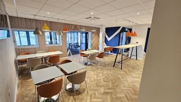 A modern dining area with multiple tables and chairs, large windows, and a herringbone wood floor.