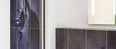 Un baño moderno con ducha, lavamanos y espejo.