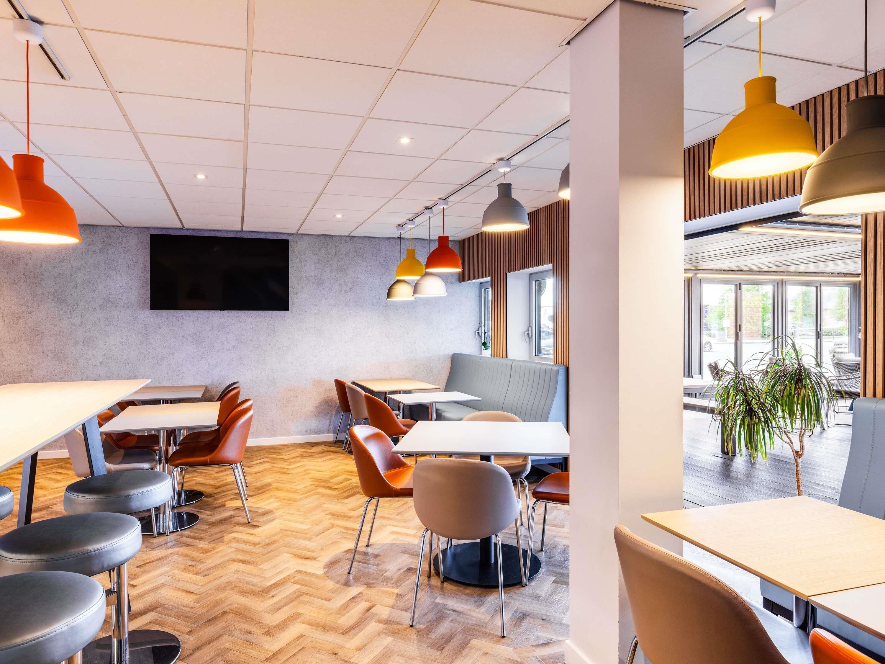 A modern dining area with herringbone patterned flooring, multiple tables and chairs, and pendant lighting.