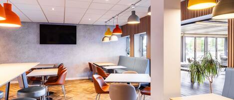 A modern dining area with herringbone patterned flooring, multiple tables and chairs, and pendant lighting.