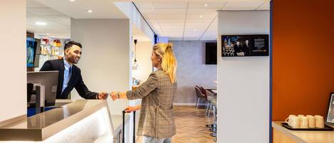 A reception area with a counter, a digital screen, and a seating area with chairs and a table.
