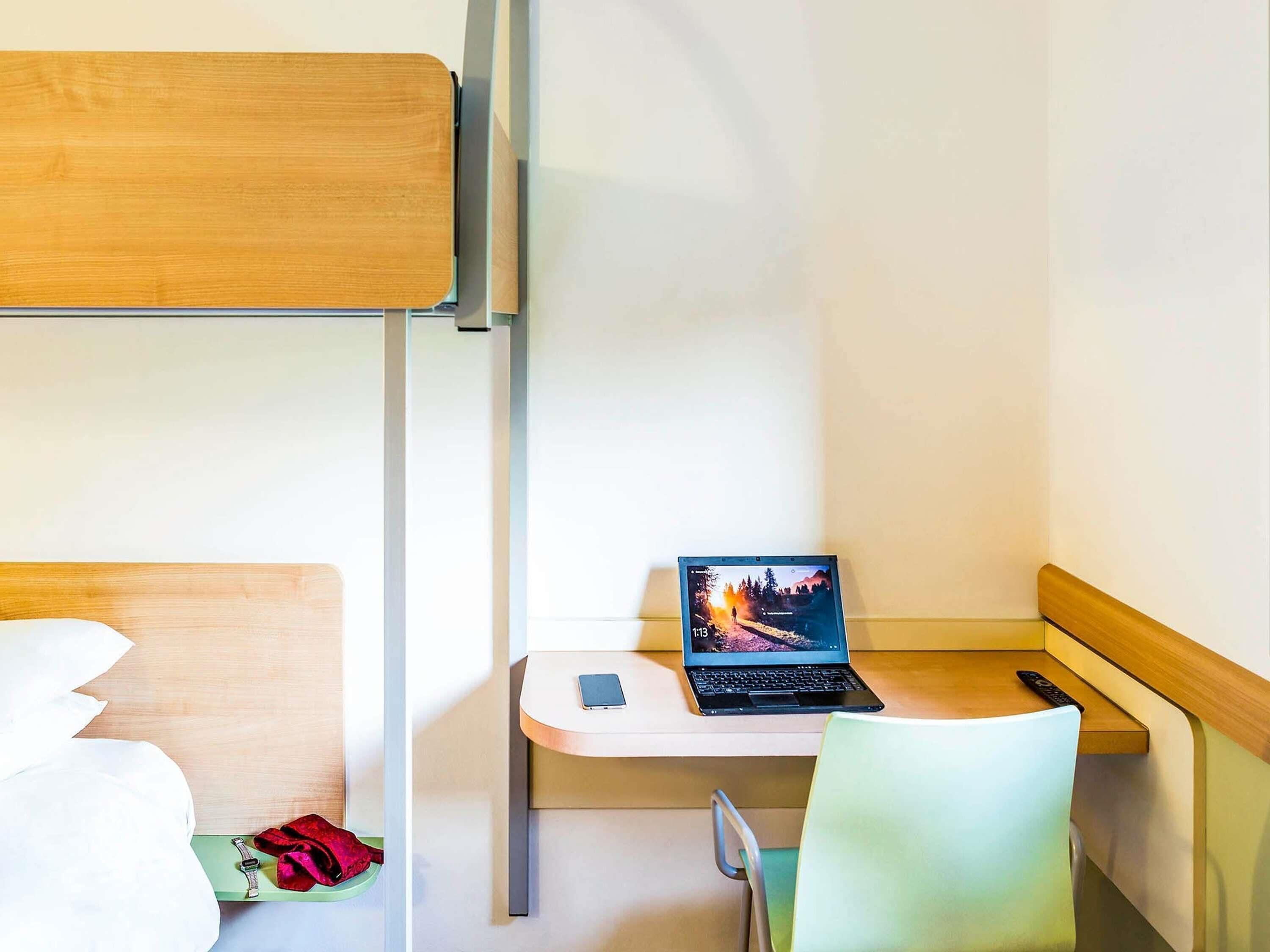 A bunk bed with a laptop on a desk, a chair, and a remote control.
