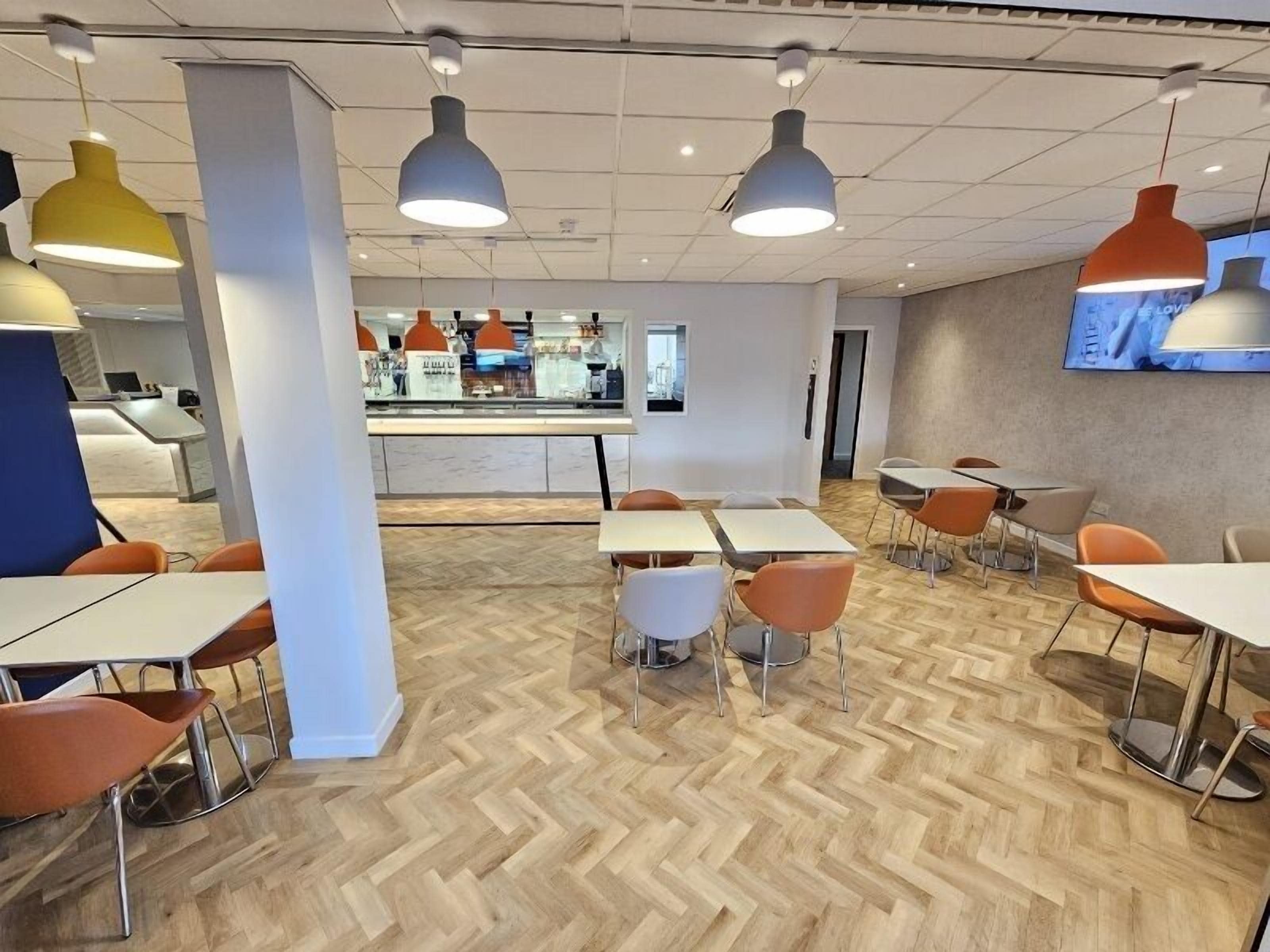 A modern dining area with wooden herringbone flooring, white tables, and orange chairs.