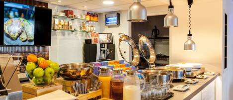 Un bufé de desayuno con diversas opciones de comida, utensilios y una máquina de café.