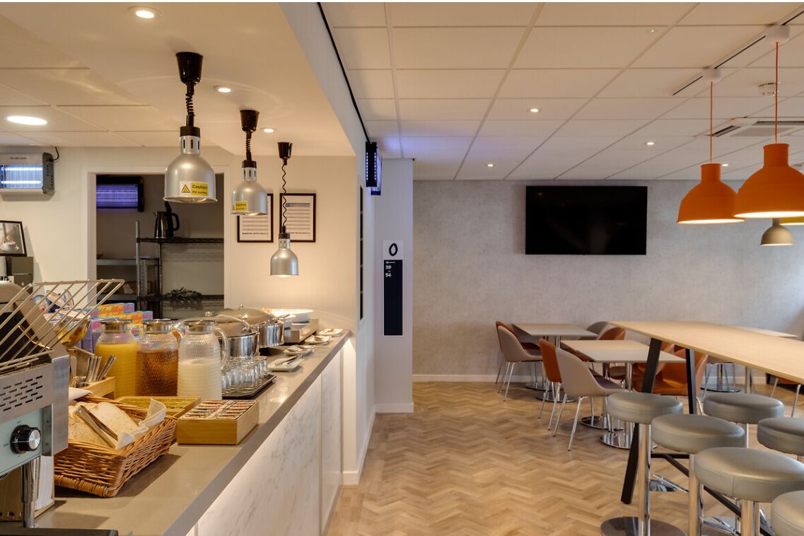 A modern cafe with a counter, seating area, and a television screen.