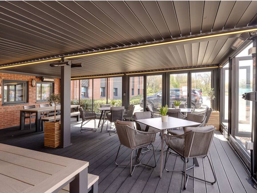 An outdoor patio area with tables and chairs, a brick wall, and large windows.