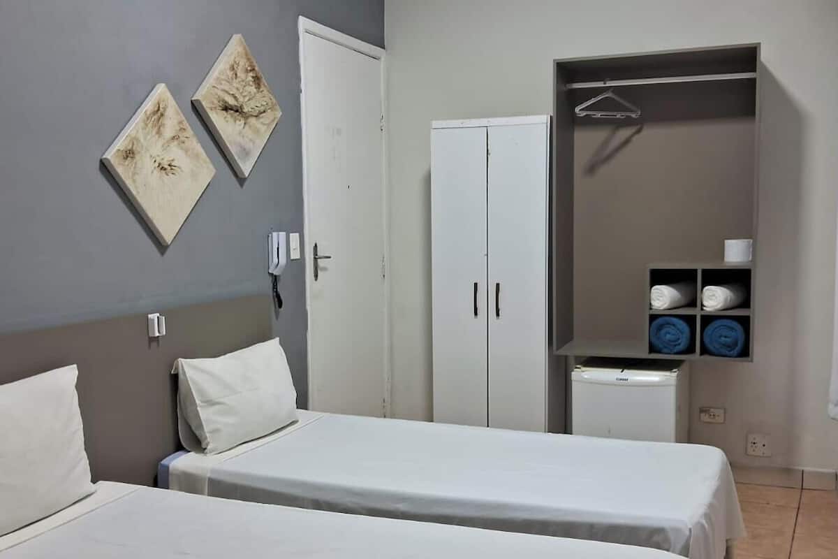 Une chambre avec deux lits, une armoire et une étagère où sont pliées les serviettes.