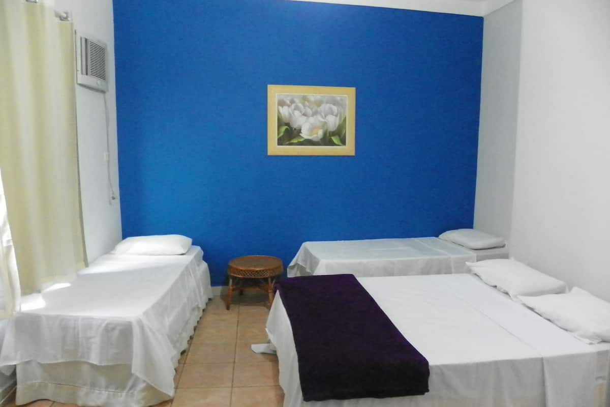 Une chambre avec deux lits simples, un petit tabouret rond, une couverture violette sur l’un des lits et un tableau représentant des fleurs accroché au mur.