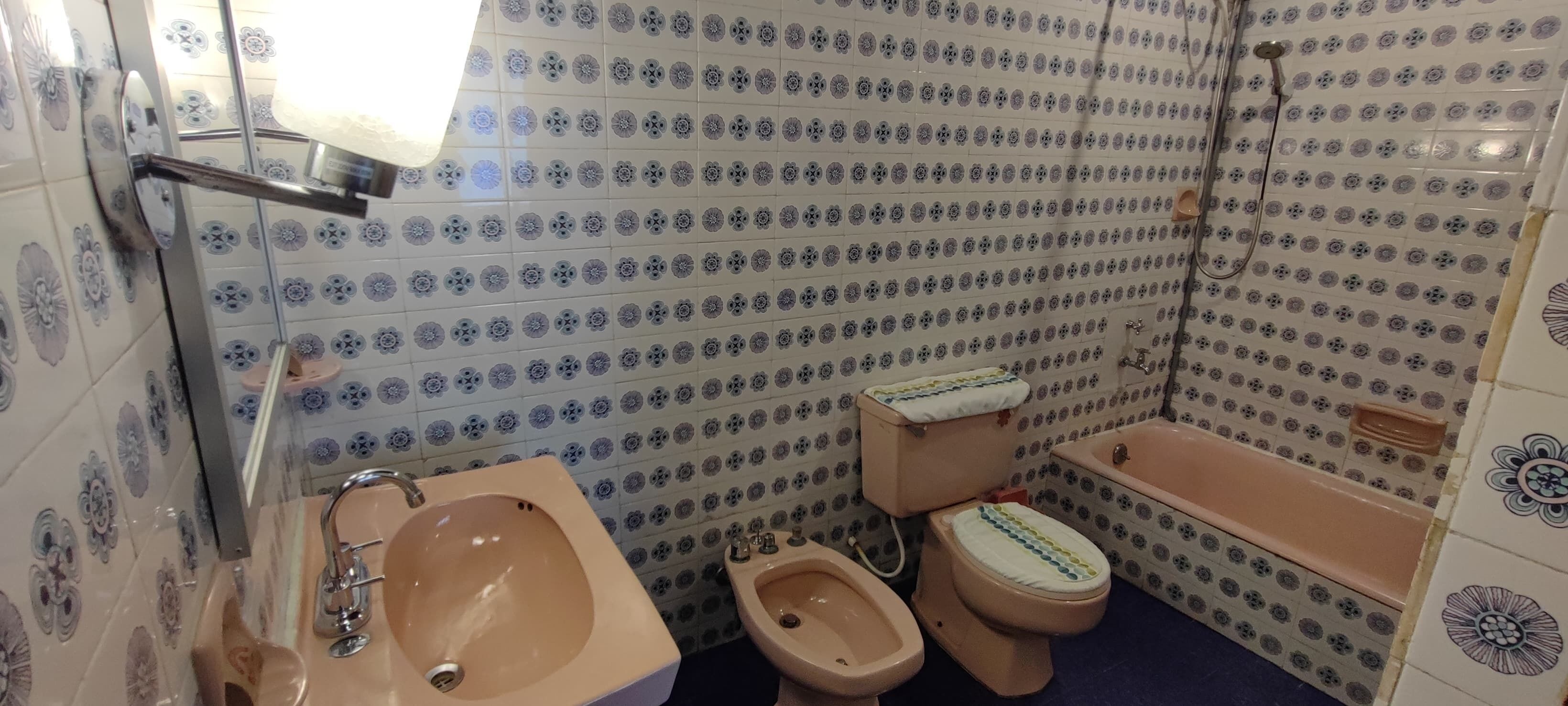 Un baño con lavamanos, bidé, inodoro y bañera, todos con un diseño de azulejos de motivos florales.