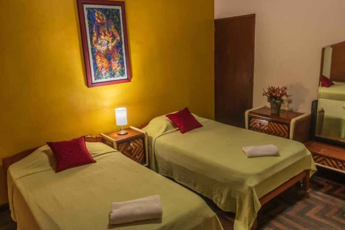 A hotel room with two beds, a nightstand with a lamp, a wooden wardrobe, and a mirror.
