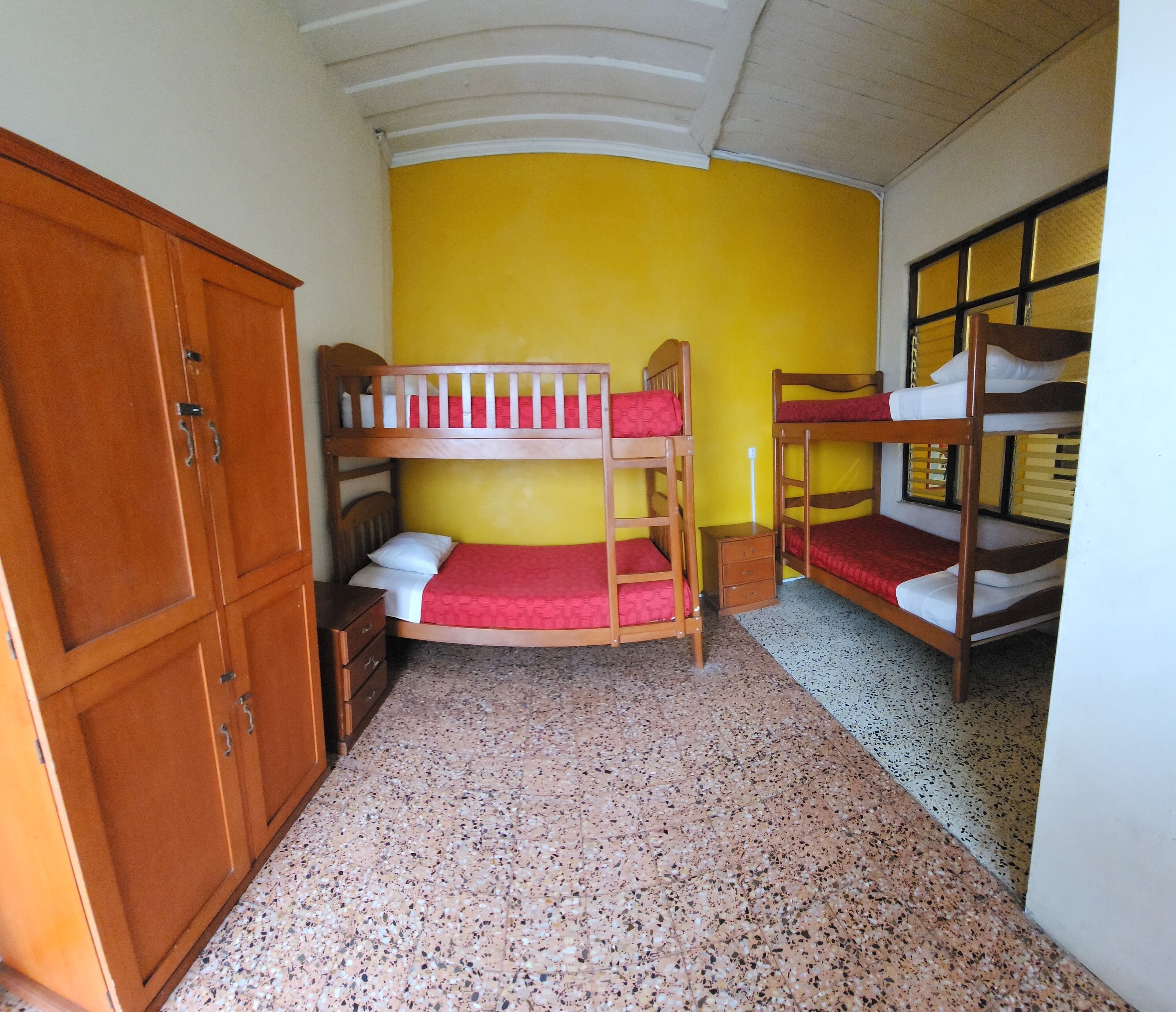 A dormitory room with bunk beds, wooden wardrobe, and a tiled floor.
