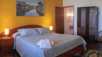 Habitación de hotel con cama, dos lámparas de noche, un cuadro en la pared, un armario y una alfombra estampada.
