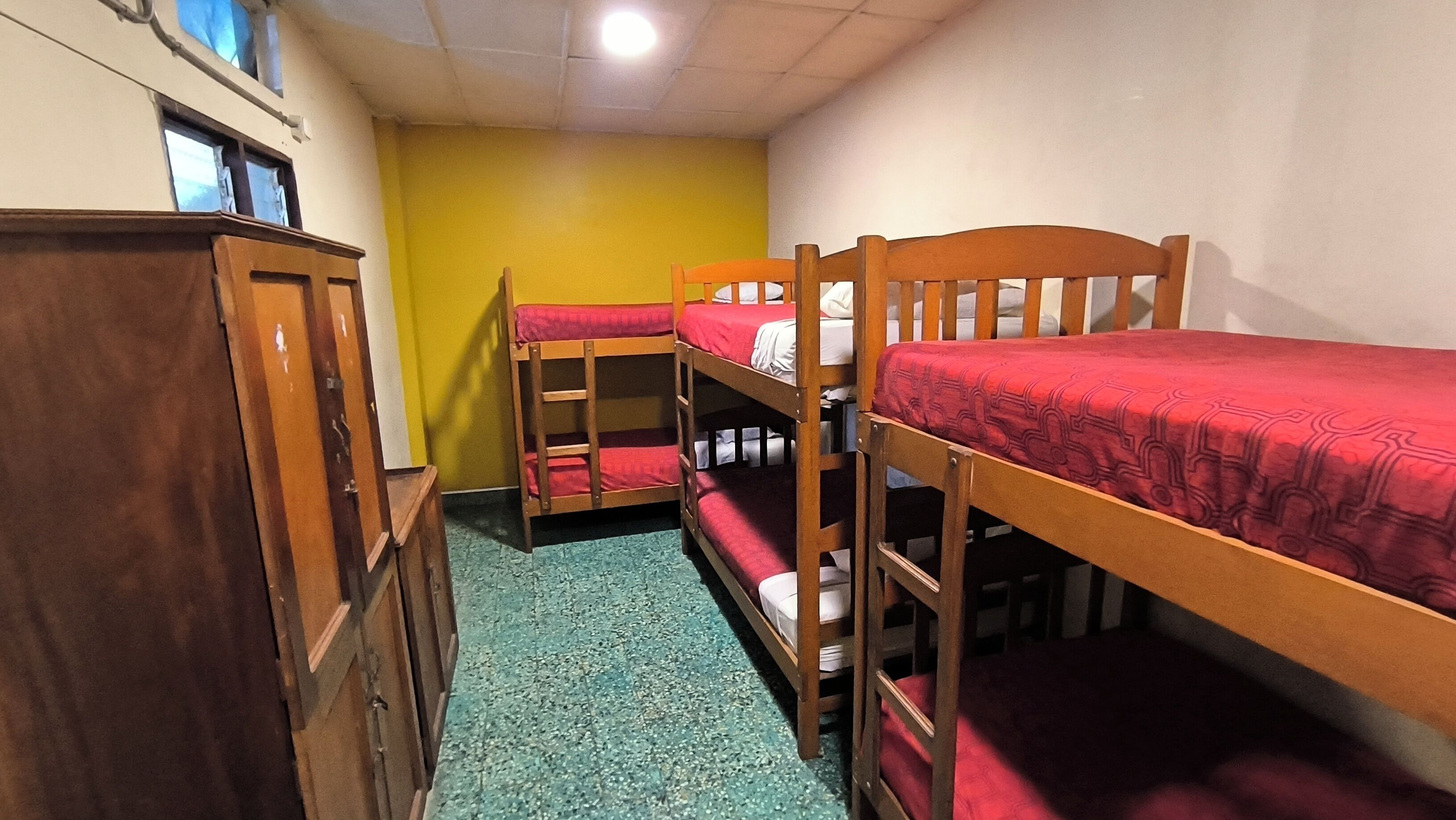 A dormitory room with bunk beds, a wooden wardrobe, and a green carpet.